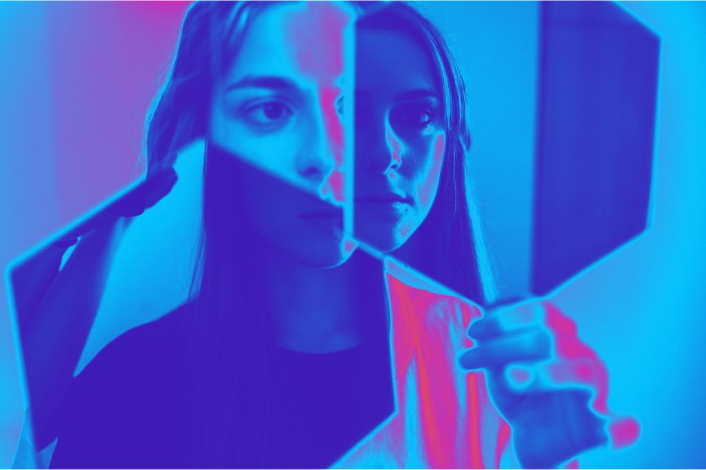 What is Shadow Work? Close-up of a female-appearing person with long hair, holding up two cubes, showing their reflection in them. The image has a blue filter with heatmap accents in pink.