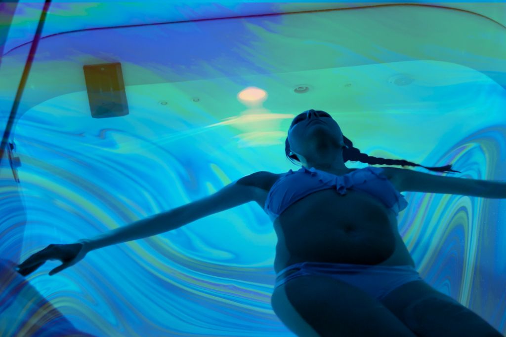 Mystical Experiences. An image of someone in the suggestion of a sensory deprivation tank. The image is blueish and dark, with some psychedelic patterns in the water.