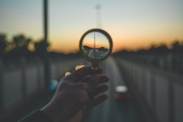 Can Ayahuasca. A person's hand holding a magnifying glass above an out of focus highway, bringing cars in the distance into focus. 