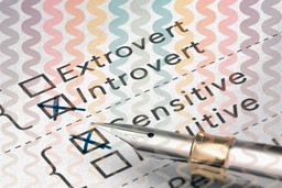 Personality Traits. 3D illustration of a personality test, with four options with checkboxes visible. In order from top to bottom, these are 'Extrovert,' 'Introvert,' 'Sensitive,' and 'Intuitive'. There is a fountain pen marking off options. Introvert and Sensitive are marked off. There are also faded, wavy zig-zag colorful lines over the image in a vertical direction, with this fading toward the bottom of the image. 