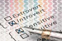 Personality Traits. 3D illustration of a personality test, with four options with checkboxes visible. In order from top to bottom, these are 'Extrovert,' 'Introvert,' 'Sensitive,' and 'Intuitive'. There is a fountain pen marking off options. Introvert and Sensitive are marked off. There are also faded, wavy zig-zag colorful lines over the image in a vertical direction, with this fading toward the bottom of the image. 