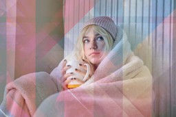 Ketamine. Image of a female-presenting person with straight blonder hair leaning against a radiator. They are wearing a soft pink beanie, are wrapped in a blanket, and are holding a mug of presumably a hot beverage. There are geometric colourful shapes overlaid over the image.