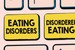 How Disordered Eating Isn’t The Same as an Eating Disorder. Image is of a close up of some keyboard keys. The background is peach, with a couple of black outlines of the keys. Two of the keys are a deep, dusty yellow. The one on the left reads &quot;Eating Disorders&quot; and the one on the right reads &quot;Disordered Eating&quot;.