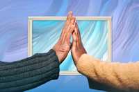 Therapeutic touch. A photograph of a hand from each of two people held up to each other. The person on the left is wearing a dark blue-grey jersey, and the one on the right is wearing a mustard yellow one. In the background is a marbled purple, blue and whte background with a white frame around part of it.