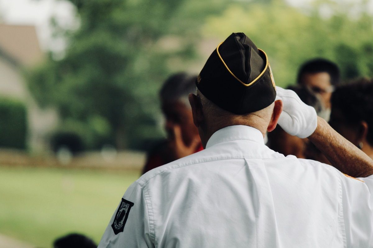 Elder solider in uniform with his back to the viewer, saluting, by Sydney Rae