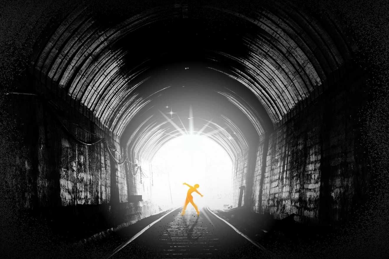 The power of darkness. The image depicts the interior of a dark tunnel with a bright white light at its end, creating a striking contrast. The tunnel walls are textured, showing rugged details in shades of black and gray. At the center, near the light source, is the silhouette of a glowing orange human figure in a dynamic pose, standing on railroad tracks that lead out of the tunnel. The composition directs the viewer's eye from the dark surroundings toward the light, emphasizing the figure as a focal point. The overall mood is dramatic and symbolic, blending darkness and illumination effectively.