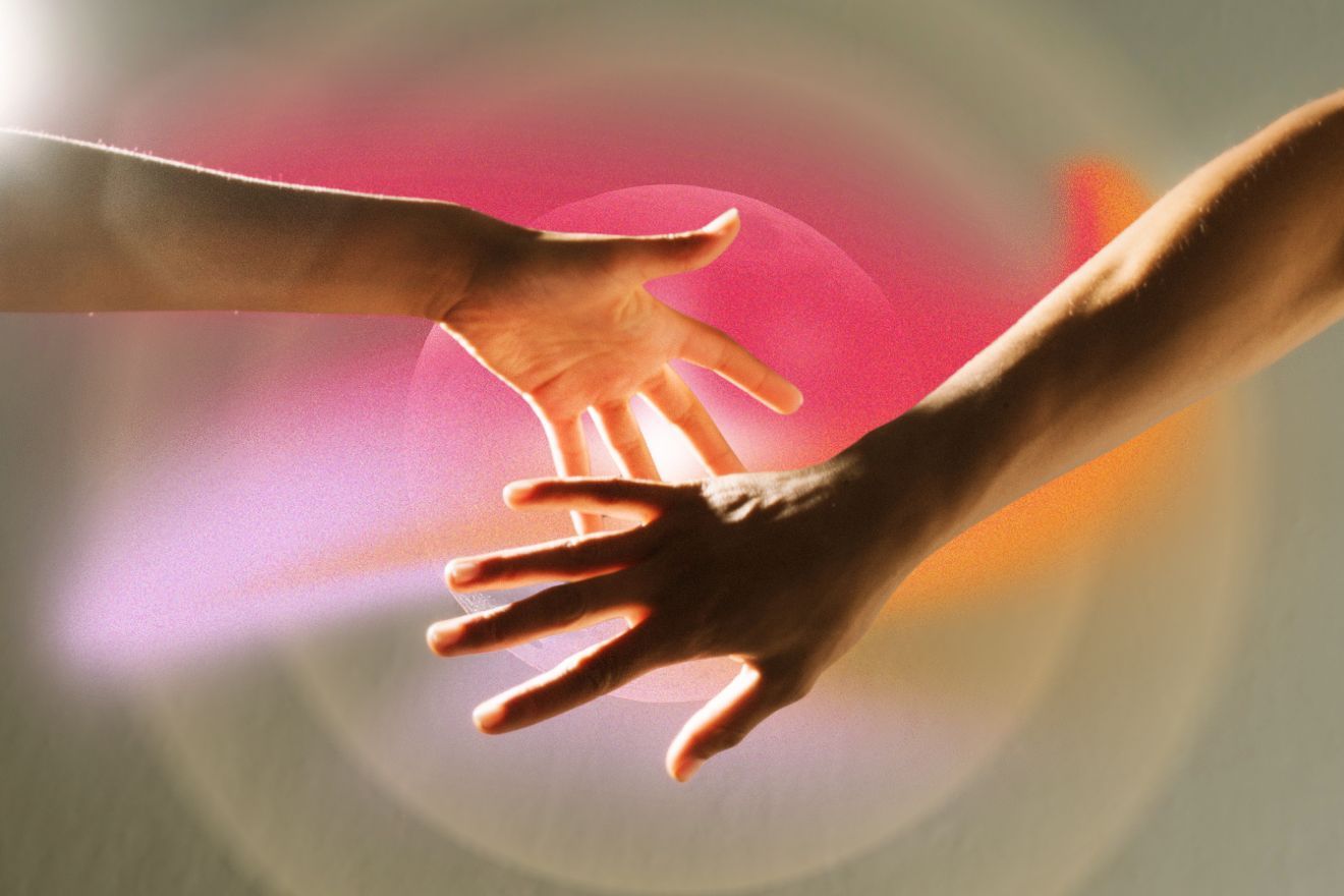 MDMA-assisted group therapy. Two outstretched hands reach toward each other in the centre of the frame, surrounded by a glowing, circular light in warm pinks, oranges and purples, creating a soft, radiant composition that suggests connection, healing, and emotional support.