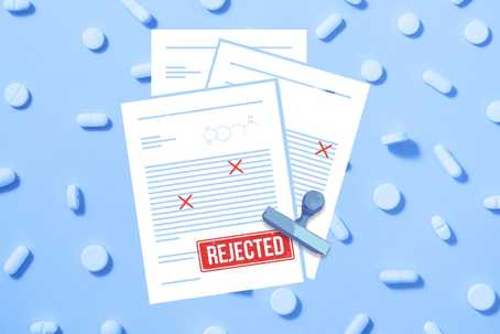 FDA's decision. A top-down view of documents with a large red 'REJECTED' stamp on a blue background with pills scattered around, scientific document, rejection letter, failed medicine