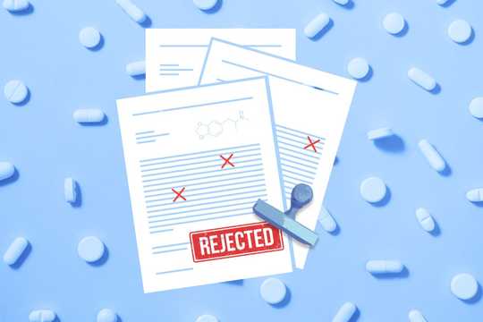 FDA's decision. A top-down view of documents with a large red 'REJECTED' stamp on a blue background with pills scattered around, scientific document, rejection letter, failed medicine