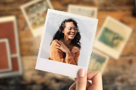Autobiographical memory. The image shows a hand holding a Polaroid-style photo featuring a woman with dark hair, wearing a warm-toned, textured, orange-brown sweater. Her face is pixelated for anonymity, but her broad smile and crossed arms suggest a joyful, relaxed moment. The background of the Polaroid is a light, neutral wall, while the scene behind the photo is a wooden surface scattered with other blurred photographs, suggesting nostalgia or memory. Warm, earthy tones dominate the color palette, with a soft focus and vignette effect enhancing the intimate, reflective atmosphere of the composition.