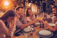 Why Someone Who Looks Healthy May Have An Eating Disorder. Image is a warm-feeling setting of a group of 5 friends sitting around a table outside around sunset. 4 of the friends are raising a toast, whereas the one person in the left foreground is sitting with their head in their hands.
