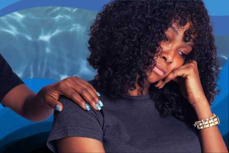 Search for Purpose. Image of a person from the shoulders up, sitting with their head resting on their hand. They are not smiling. They have brown skin, black curly shoulder-length hair, and are wearing a dark blue t-shirt. There is another person's comforting hand on their shoulder. The background is a blue water-like pattern.
