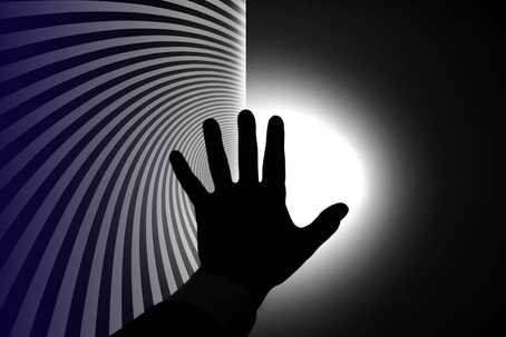 Near-Death and Psychedelic Experiences. The image features a silhouetted hand reaching towards a bright white light at the center-right, creating a strong contrast against a dark background. The left side of the image has a hypnotic spiral pattern of alternating dark and light grey lines that converge towards the light, drawing the eye inward. The hand is in the foreground, with fingers spread, and its dark silhouette is sharply outlined against the glowing white light, giving the scene a surreal and dramatic quality. The color scheme is monochromatic, dominated by black, grey, and white tones.