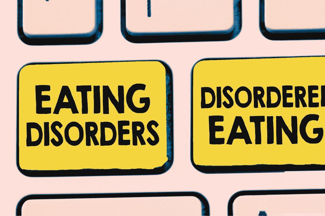 How Disordered Eating Isn’t The Same as an Eating Disorder. Image is of a close up of some keyboard keys. The background is peach, with a couple of black outlines of the keys. Two of the keys are a deep, dusty yellow. The one on the left reads "Eating Disorders" and the one on the right reads "Disordered Eating".