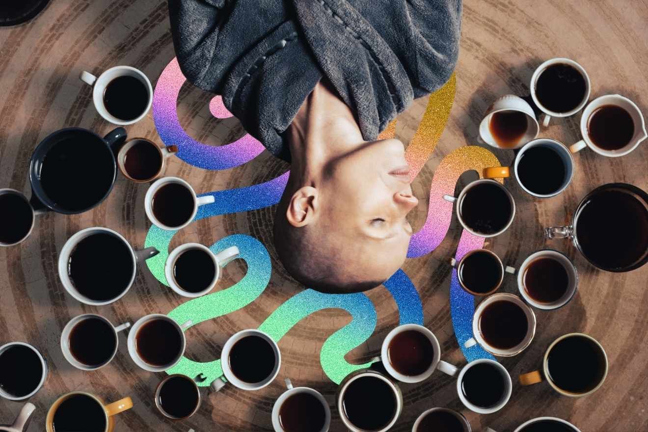 Addiction Recovery. The image features a person with a shaved head lying on their back with their head tilted upside down, eyes closed, and wrapped in a textured gray robe. Surrounding them is an array of coffee cups filled with dark liquid, scattered in an organic arrangement on a wooden surface. Among the cups, a vibrant, iridescent, and wavy path in shades of blue, green, purple, and gold flows through the scene, adding a surreal and dreamlike quality. The contrast between the warm, earthy tones of the wood and coffee and the glowing, psychedelic colors creates a visually striking composition.