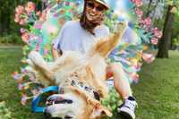 Psychedelics and Animals. A photo of a person siting on the grass in with a golden labrador lying upside down in front of them. There are dreamy colorful flowers behind the person.