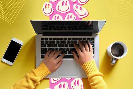 Article About LSD. A top-view of someone working at a laptop. The tabletop is yellow, and there is a vertical pink strip directly beneath the laptop with trippy off-white smiley faces scattered throughout the graphic pattern. There is a cellphone to the left of the person, and a cup of coffee to the right. There are geometric outline patterns in the top left and top right corners.